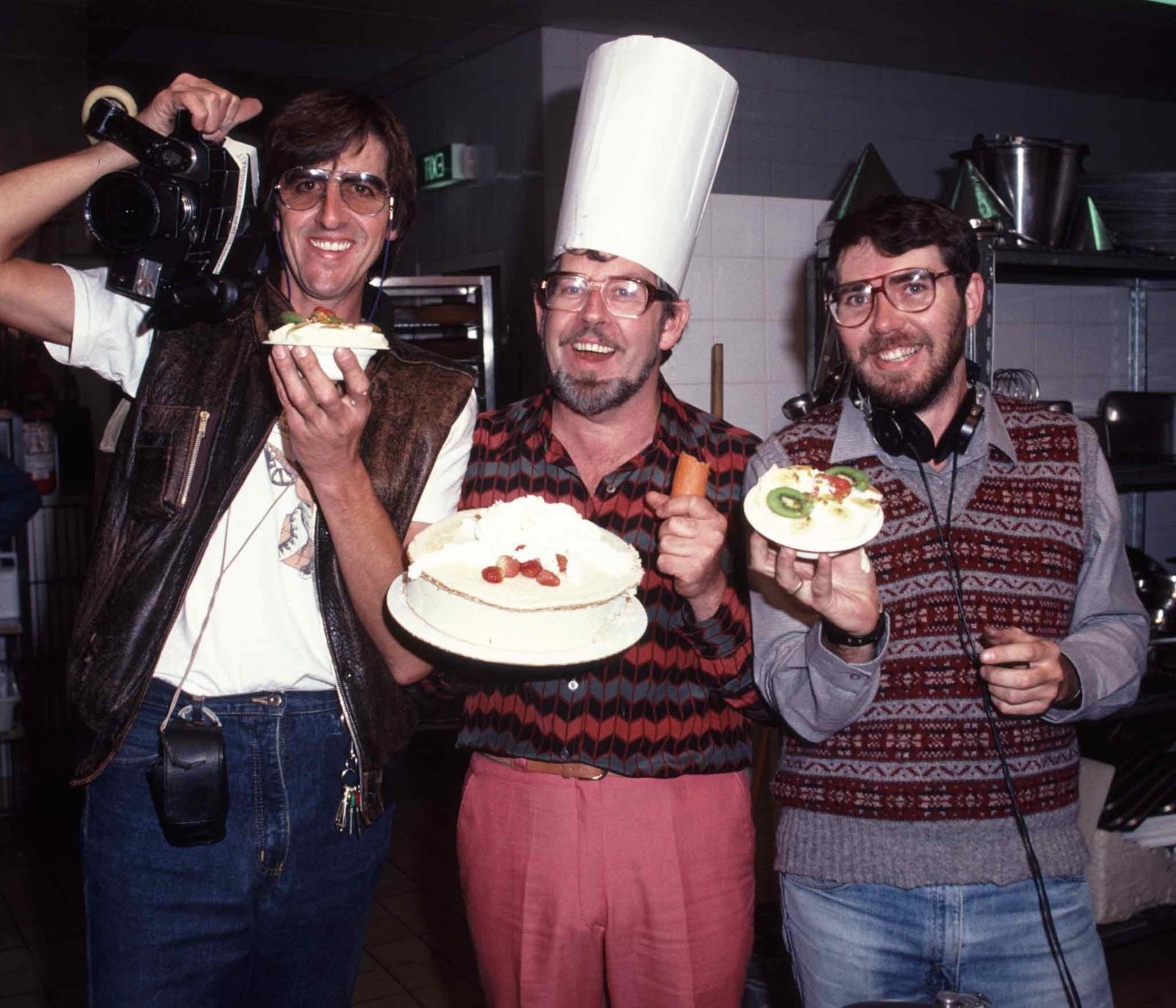 A Wonder World camera crew on location, two crew with camera and headphones beside a chef holding a pavlova