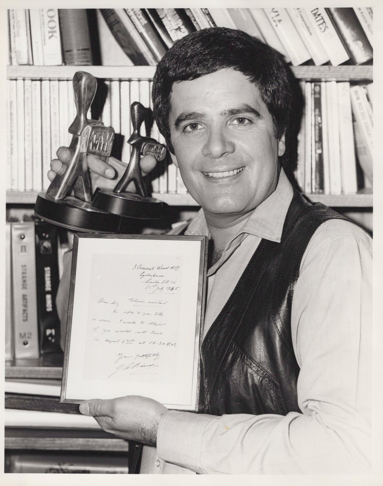 Simon Townsend holding two TV Week Logie Awards beside a framed 1925 letter handwritten by John Logie Baird