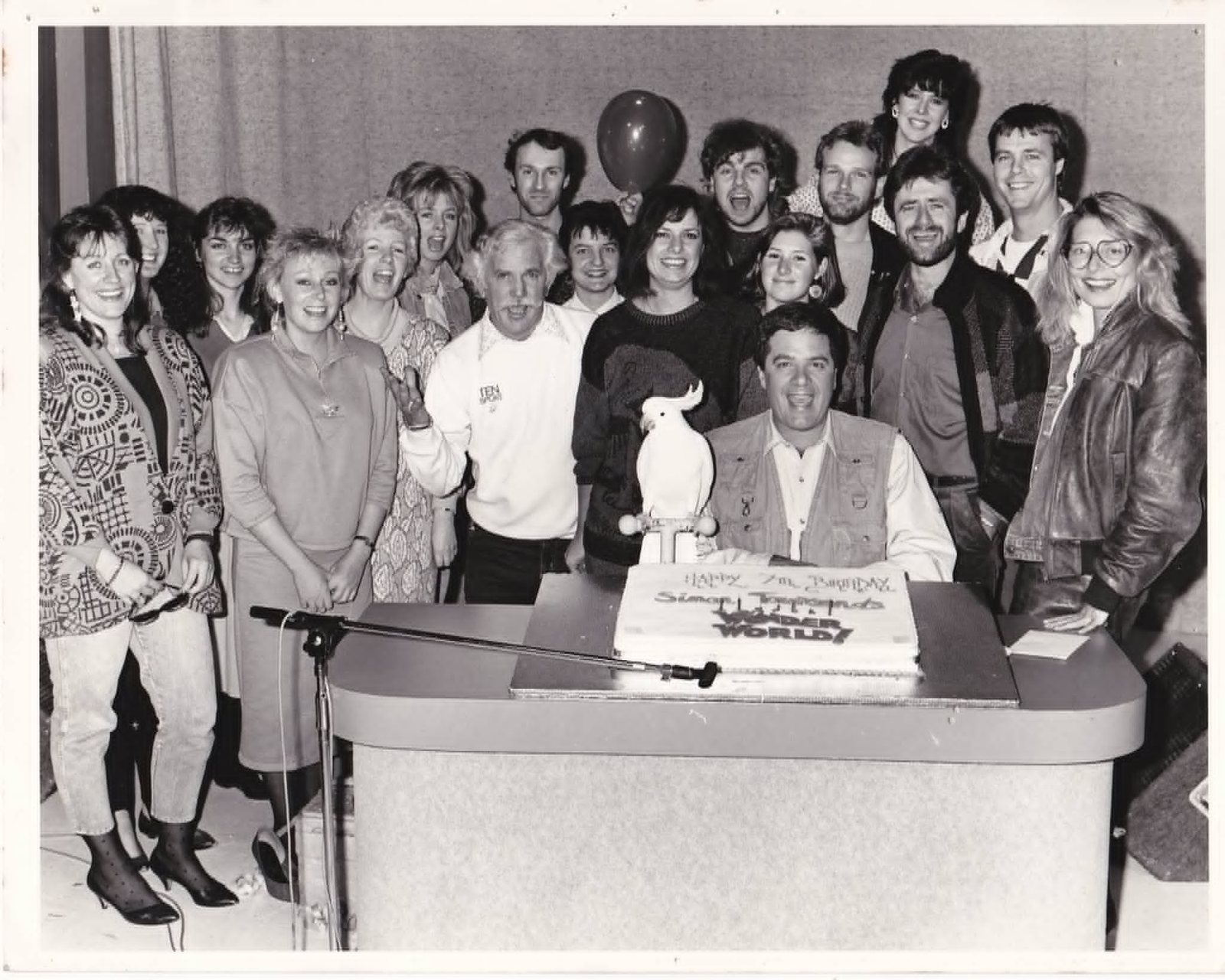The Wonder World cast and crew gathered around the Happy 7th Birthday cake in 1986, Simon Townsend seated with the show's cockatoo on a perch